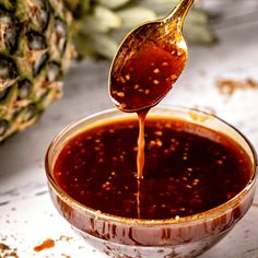 a spoon full of sauce being poured into a bowl with pineapples in the background