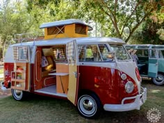 an old vw bus is parked in the grass with other vans behind it and trees