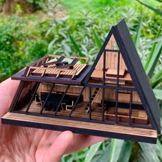 a hand holding a model of a house in it's palm tree - lined yard