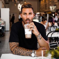 a man sitting at a table with a drink in his hand and tattoos on his arm