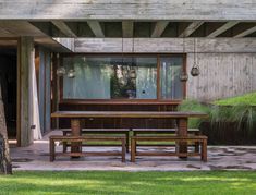 a wooden table and bench in front of a building with large windows on the side