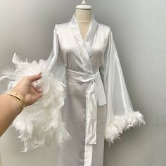 a white robe with feathers on it being held up by a woman's hand