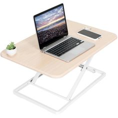 an open laptop computer sitting on top of a wooden table next to a white plant