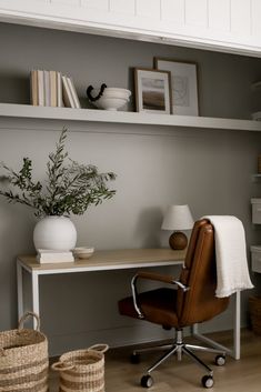 a desk with a chair, lamp and vase on it in front of a book shelf