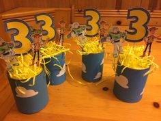 three tin canisters filled with cupcake toppers and yellow streamers on the table