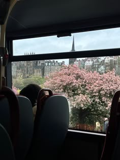 the view from inside a bus looking out onto a city with pink flowers on it