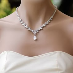 a woman wearing a white dress with a diamond necklace on her neck and an earring in the shape of a flower