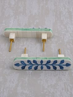 two blue and white wall hooks with gold handles on a gray background, one has a green leaf design