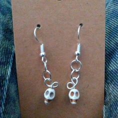 a pair of silver earrings with skulls hanging from it's earwires in front of a card