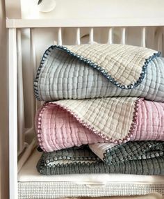 a stack of folded blankets sitting on top of a white shelf next to an open drawer