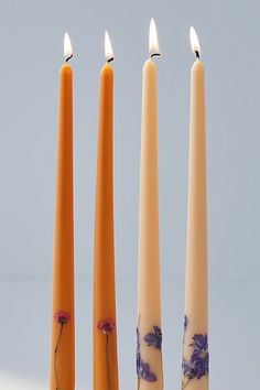 three candles with flowers on them sitting in front of each other and one candle is lit