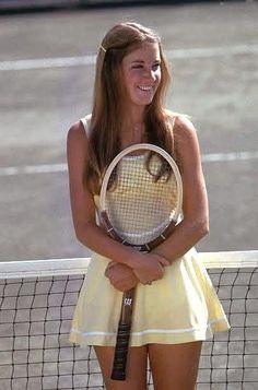 a woman standing on a tennis court holding a racquet and smiling at the camera