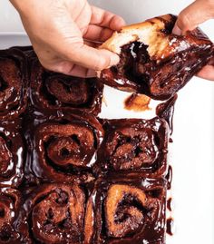 someone is holding a piece of chocolate roll in front of the brownie squares that are on top of each other