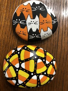 two painted rocks sitting on top of a wooden table covered in black, white and orange cats