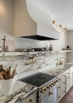 a kitchen with marble counter tops and gold faucets on the stove top, along with white cabinets