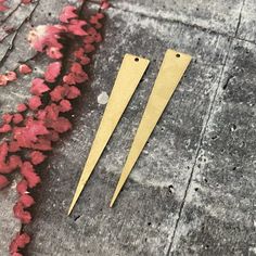 two pairs of long gold earrings sitting on top of a cement floor next to red flowers