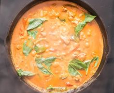 a skillet filled with soup and vegetables on top of a stove burner covered in green leaves