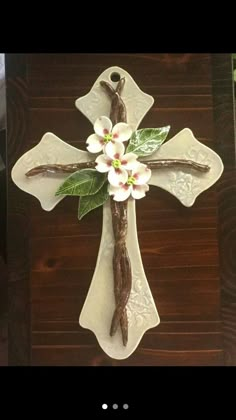 a cross with white flowers and green leaves on it sitting on top of a wooden table