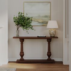 a table with a plant on it and a lamp next to it in front of a painting