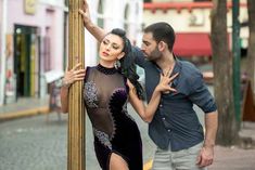 a man standing next to a woman leaning on a pole