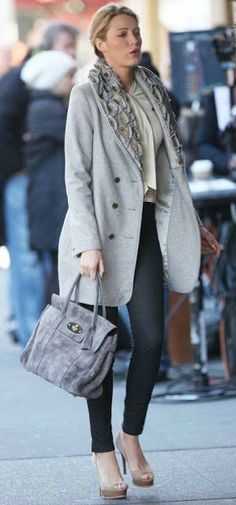 a woman walking down the street carrying a gray purse