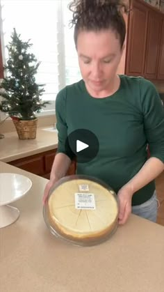 a woman is holding a pie in her hands and looking at the pie on the counter