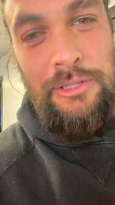 a close up of a person with a beard wearing a black shirt and looking at the camera