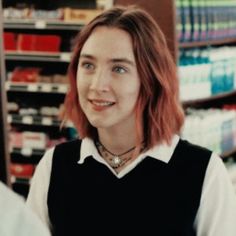 a woman with red hair is standing in front of a store shelf and smiling at the camera