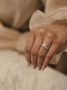 a woman's hand with two wedding rings on her left and the other hand holding an engagement ring