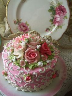 a pink and white cake with flowers on it sitting on a table next to plates