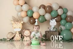 a baby sitting in front of a cake surrounded by balloons and jungle themed decorations on the wall