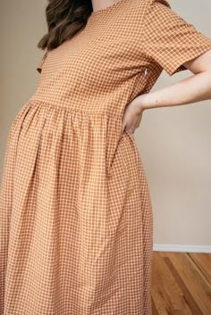 a woman standing in front of a wall wearing an orange and white checkered dress