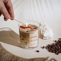 a person lighting a candle in a glass with coffee beans and sugar on the side