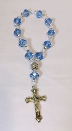 6” Rosary Overflowing Blue-Transparent Multifaceted Glass Beads and Crucifix This beautiful 6-inch bracelet is perfect for any occasion, whether it's Mother's Day, Christmas, birthdays, Valentine's Day, or Confirmation/Communion. The bracelet features 11 stunning blue and multicolored glass beads in a round shape, each measuring .375 inches in width, and one metal bead. The 11 blue beads are multifaceted, adding an extra touch of elegance. The bracelet also has a charming crucifix as a centerpiece, to complete the religious theme. It is held all together by elastic material for a comfortable fit making it easy to slip-on and pull-off. This item is perfect for those who love religious-themed jewelry and makes a great gift. Rosary stretch bracelet, with blue main beads with silver beads in b How To Make A Rosary, Diy Rosary Bracelet, Diy Rosary Necklace, Rosary Ideas, Beautiful Rosaries, Diy Rosary, Rugged Rosary, Catholic Rosary Bracelet, Anglican Rosary