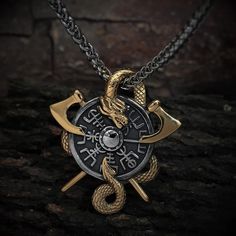 a gold and black necklace with two crossed swords on it, sitting on a rock