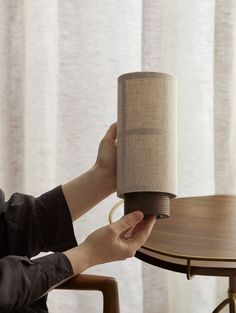 a woman holding up a lamp on top of a wooden table next to a window