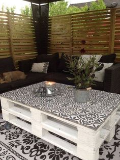 an outdoor living room with black and white patterned rugs, couches, coffee table and wooden slatted privacy screens