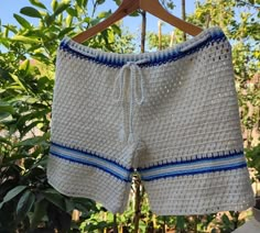 a crocheted shorts hanging on a wooden hanger in front of some trees