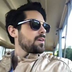 a man wearing sunglasses is sitting on a bus and looking at something in the distance