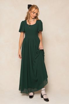 Twirl in style with the Abbie Dress in Emerald Chiffon. The flowy chiffon fabric and subtle sweetheart neckline provide a romantic touch, while the short bell sleeves and maxi-length skirt with functional pockets add a playful twist. This dress is not only the ultimate fall bridesmaids silhouette, but perfect for date night, special events, church and more. With a hidden back zipper, princess seams on the bodice and full lining, you simply can't go wrong. This women's dress is available in up to Olive Green Bridesmaid Dress Azazie, Moss Colored Dress, Bell Sleeve Bridesmaid Dress, Mennonite Bridesmaid Dresses, Dark Green Cottagecore Dress, Modest Formal Dresses Knee Length, Dress Patterns Elegant, Dark Green Dress With Sleeves, Formal Dresses Midsize