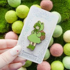 a person holding up a green frog pin