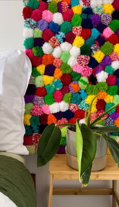 a colorful wall hanging over a bed next to a potted plant on a wooden table