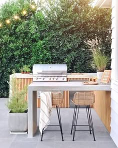 an outdoor table with two chairs and a grill in the back yard next to some bushes