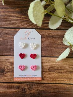 three pairs of heart shaped earrings on top of a wooden table next to a plant