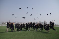 a group of people standing on top of a field with graduation caps in the air