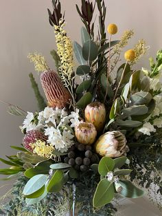 a vase filled with lots of different types of flowers and greenery on top of a table