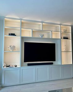 a large entertainment center with white shelves and lights on the wall, along with a flat screen tv