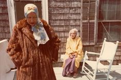 an old woman wearing a fur coat and sitting on a bench next to another older woman