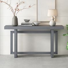 a gray table with two vases and a lamp on it next to a plant