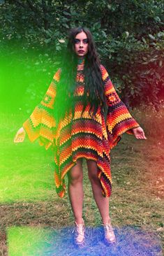 a woman with long hair standing in the grass wearing a colorful dress and white shoes